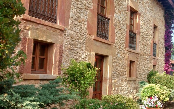 A stone building with multiple windows and a small garden area with various plants and flowers.
