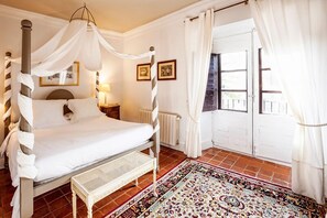 A bedroom with a four-poster bed, a bedside table, a bench, a patterned rug, and a view of the outside through a door. - Salinas de Imon (Siguenza)