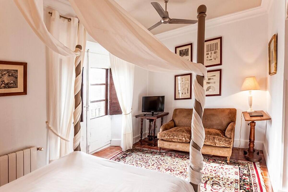 A bedroom with a canopy bed, a television, a chair, and framed pictures on the wall.