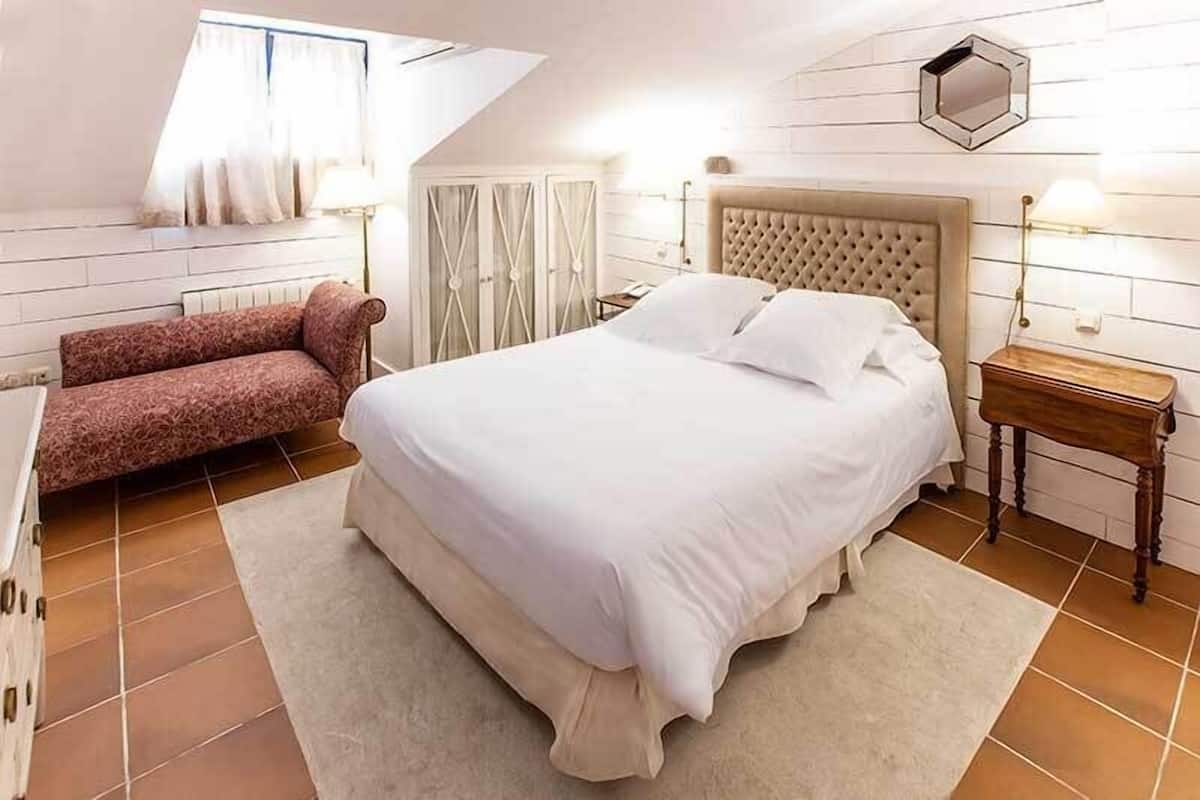 A bedroom with a large bed, a sofa, a nightstand, and a window with curtains.