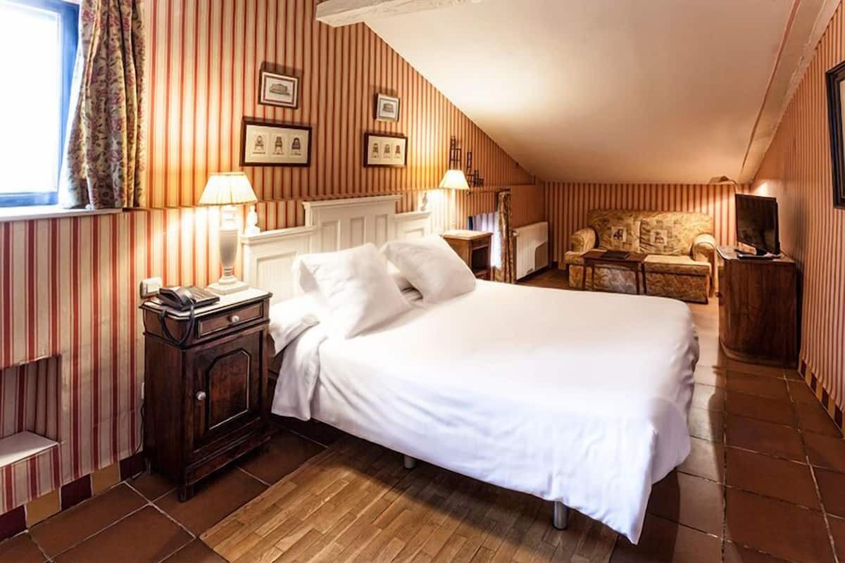 A hotel room with a large bed, a wooden nightstand, a chair, and a television.