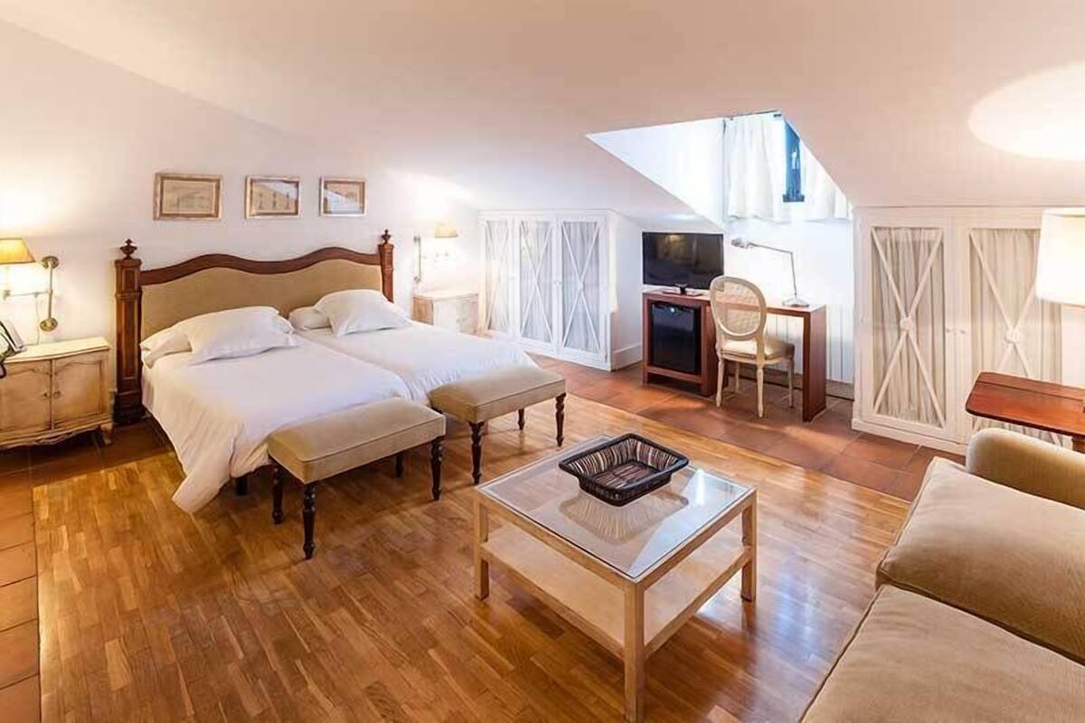 A hotel room with two beds, a desk, a TV, and a small balcony.