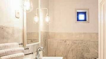 Un bany amb un mirall gran, un lavabo i un vàter. Hi ha tovalloles penjades en un suport i una petita finestra sobre el vàter.