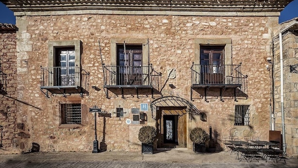 A stone building with a traditional facade, a central entrance with a door, and two balconies with railings. - Salinas de Imon (Siguenza)