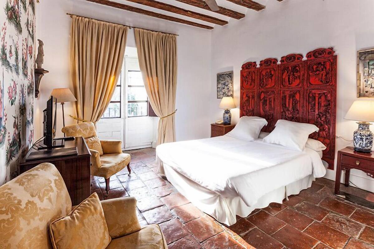 A bedroom with a large bed, a wooden headboard, a chair, a desk, and a lamp.