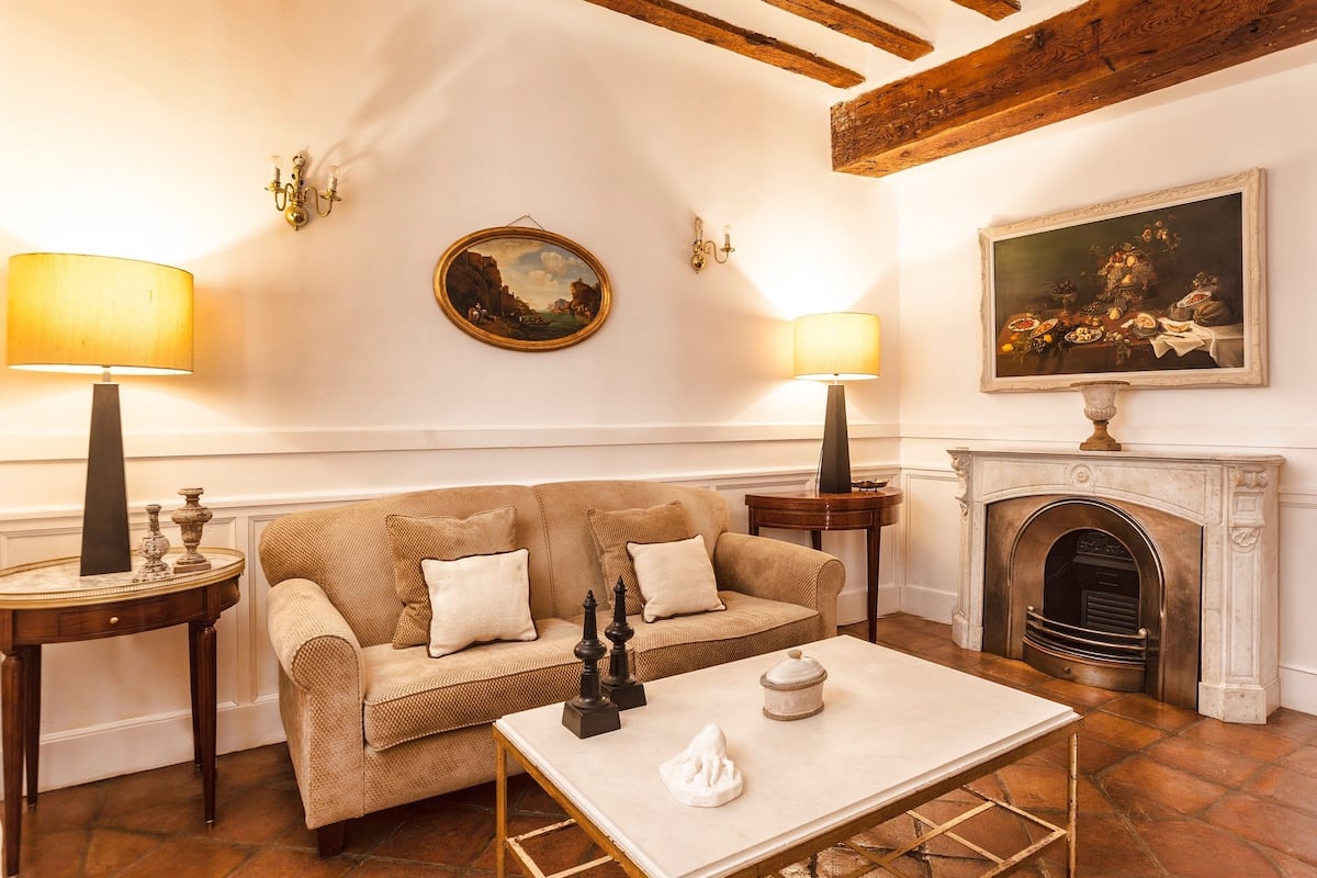 A cozy living room with a beige sofa, two side tables with lamps, a fireplace, and framed artwork on the walls.