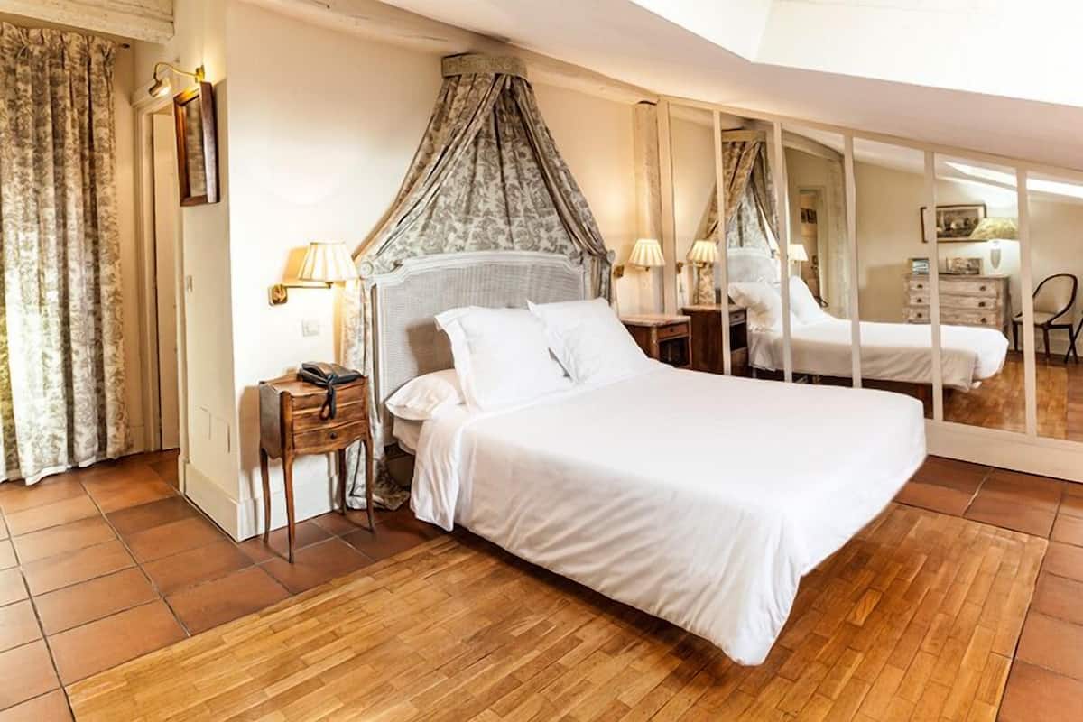 A bedroom with a large bed, a bedside table, a lamp, a mirror, and a wardrobe.