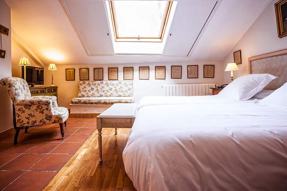 A bedroom with a skylight, a bed, a chair, a sofa, and a table.
