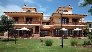 A two-story building with a balcony, outdoor seating, and a well-maintained lawn. - Rural Los Nogales (Pozo Alcon)