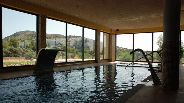 An indoor swimming pool with clear views of a mountainous landscape through large windows. - Rural Los Nogales (Pozo Alcon)