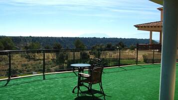 Un balcón con césped artificial verde, una mesa y dos sillas, y vistas a un paisaje boscoso.