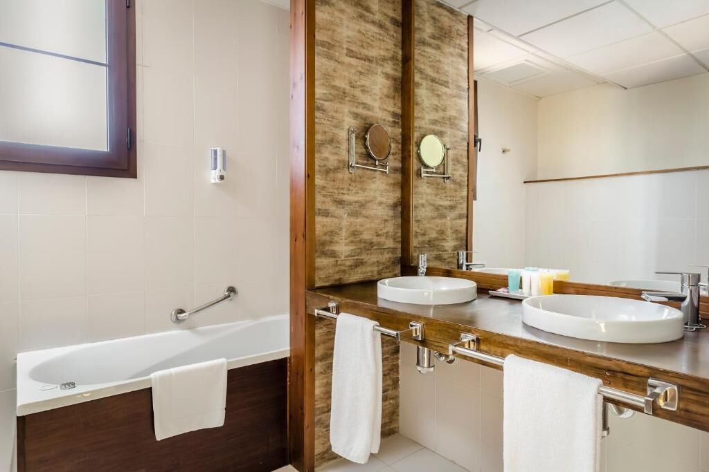 Un baño moderno con bañera, dos lavamanos y un espejo grande.