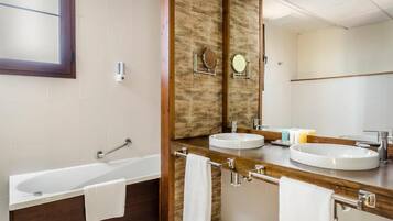 Un baño moderno con bañera, dos lavamanos y un espejo grande.