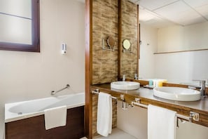 Un baño moderno con bañera, dos lavamanos y un espejo grande.
