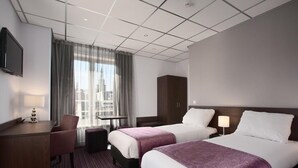 A hotel room with two beds, a desk, a chair, a TV, and a window with curtains.