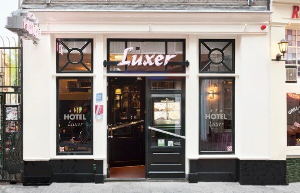 Un hotel llamado 'Luxe' con entrada negra, ventanas amplias y un letrero que indica un restaurante y parrilla.