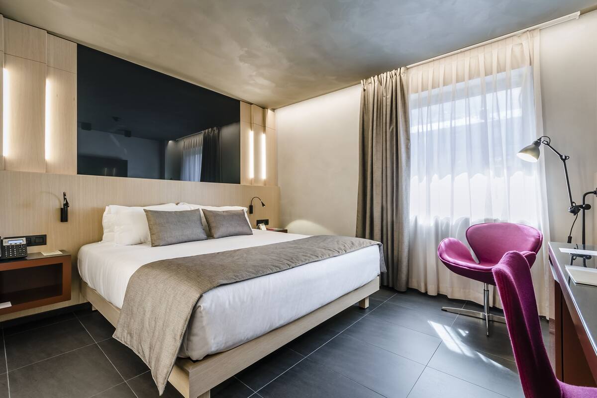 Una habitación de hotel moderna con una cama grande, mesitas de noche, un escritorio y una silla.