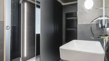 Un baño moderno con ducha de vidrio, un lavamanos blanco y un espejo con luz redonda.