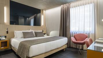 A modern hotel room with a large bed, a desk, a chair, and a mirror.