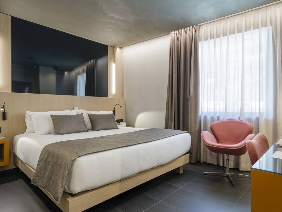 A modern hotel room with a large bed, a desk, a chair, and a mirror.