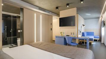 A modern hotel room with a large bed, a desk with chairs, a TV, and a shower area.
