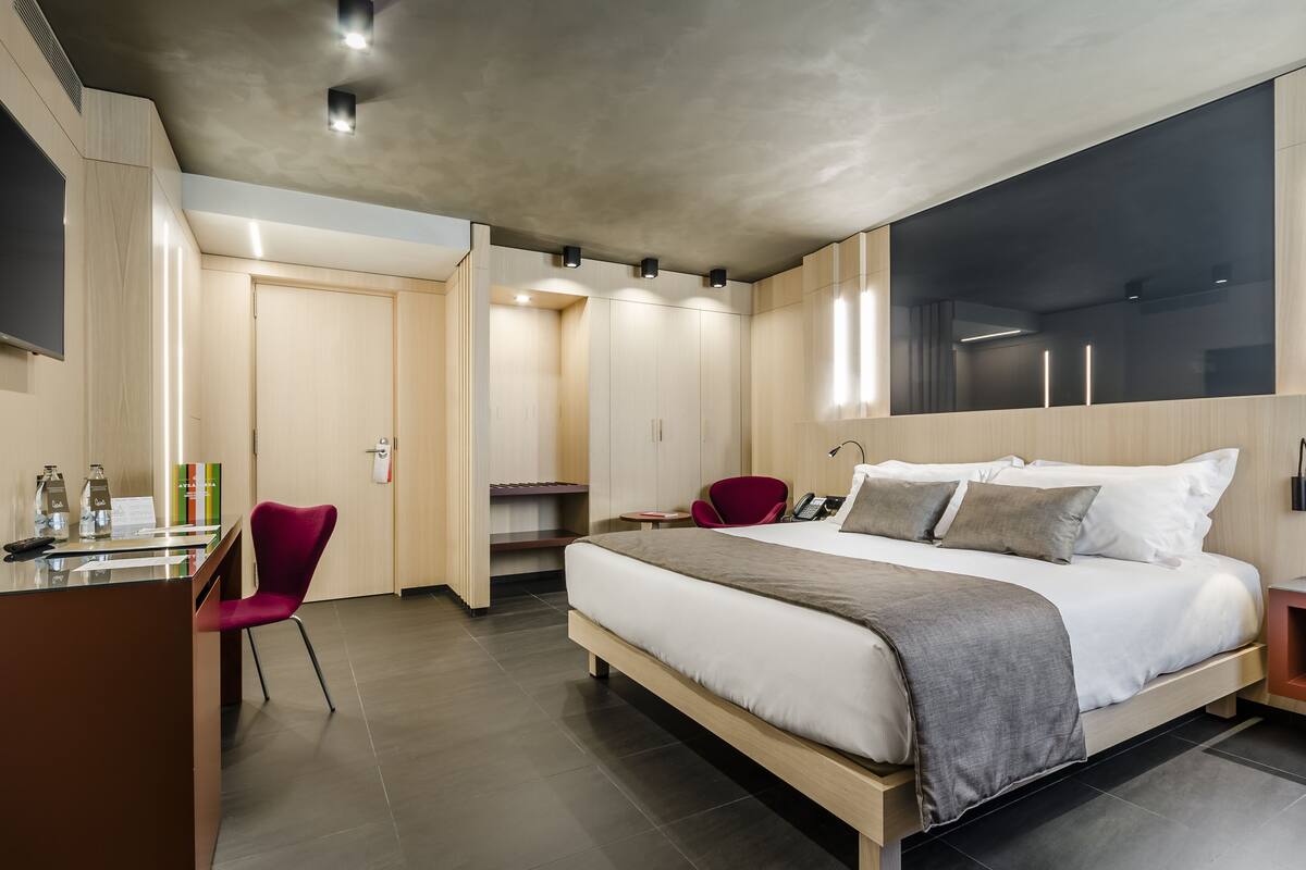 Una habitación de hotel moderna con una cama grande, un escritorio con silla y un armario.