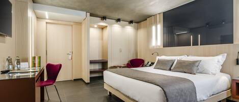 A modern hotel room with a large bed, a desk with a chair, and a wardrobe.
