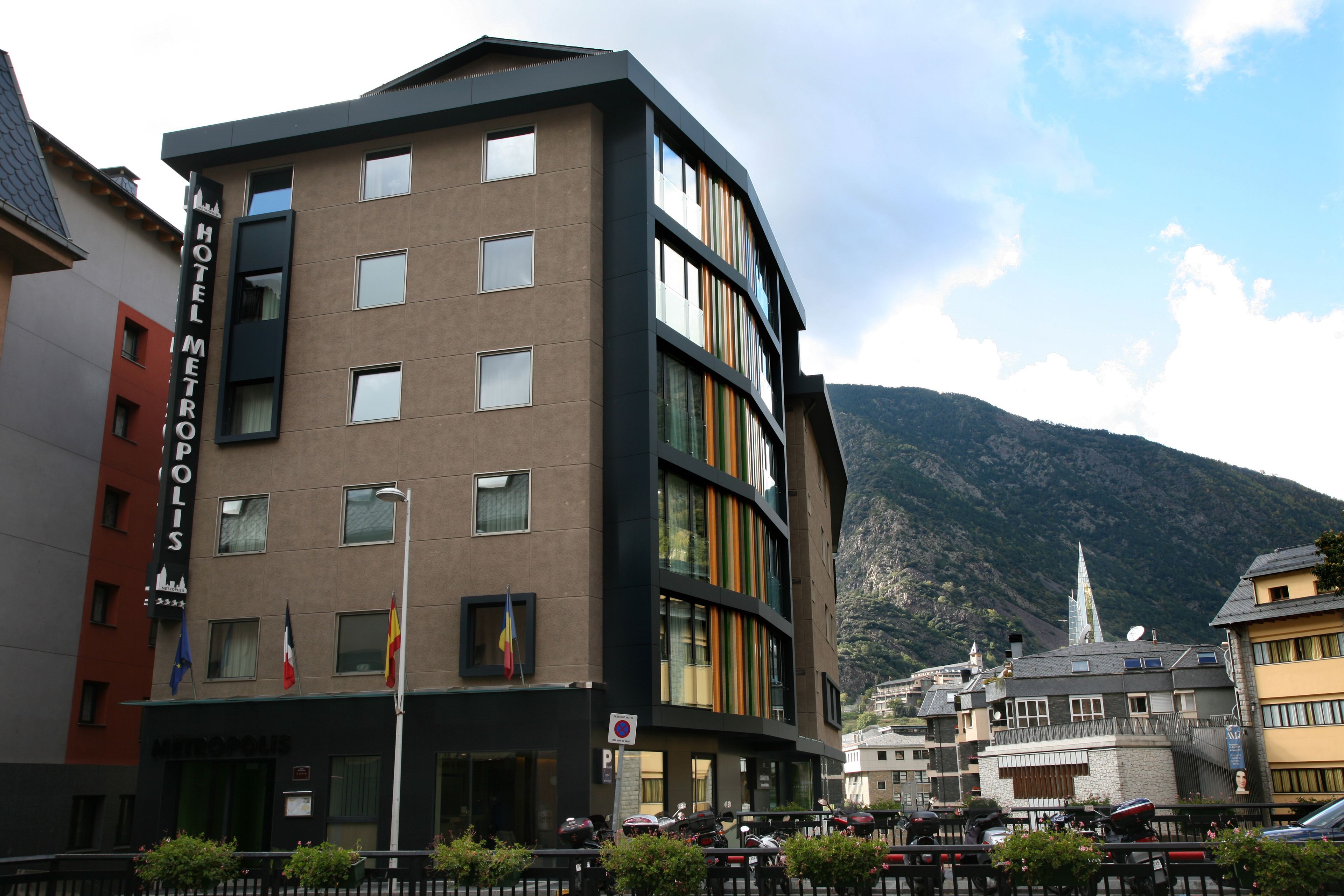 Un hotel moderno con varios pisos, amplias ventanas y montañas al fondo.