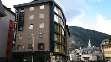 Un hotel moderno con varios pisos, amplias ventanas y montañas al fondo.