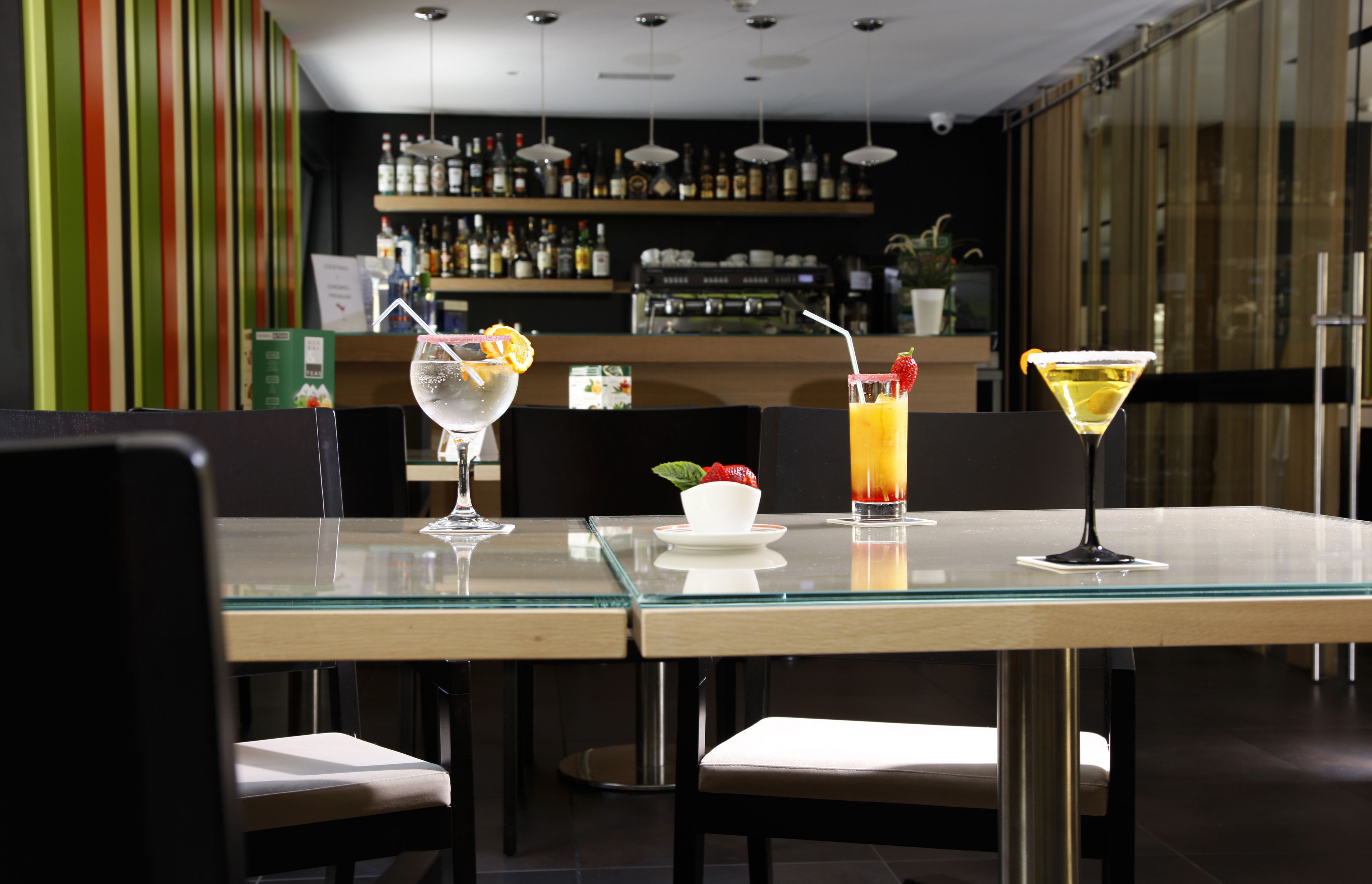 Ein stilvoller Barbereich mit einem Glastisch, gedeckt für zwei Personen, mit einem Martini und einem Cocktail mit Fruchtbeilagen.