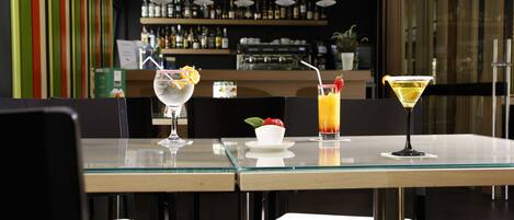 Un bar moderno con una mesa de vidrio para dos personas, mostrando un martini y un cóctel con guarnición de frutas.