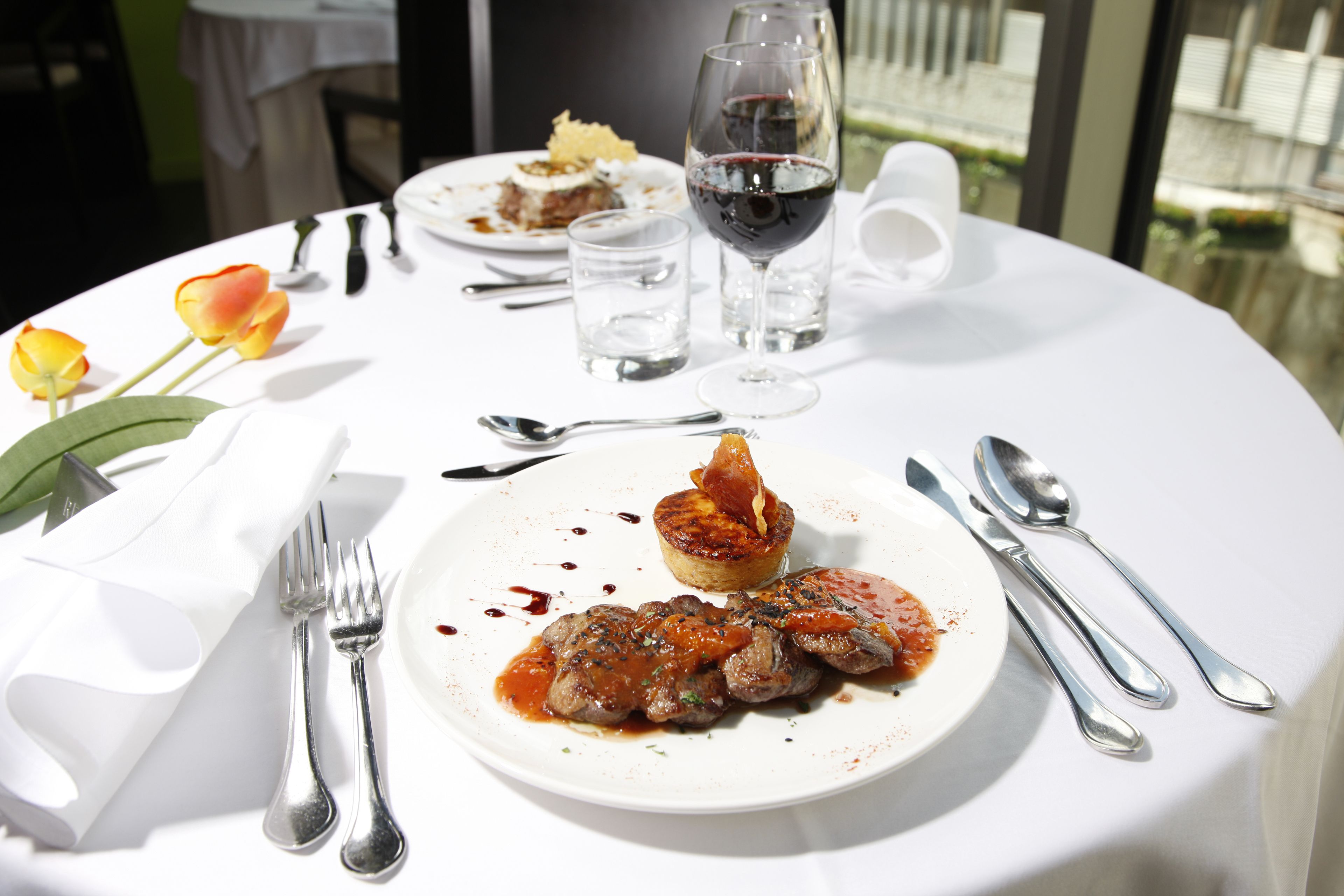 A dining table with plates of food, cutlery, and a glass of red wine.