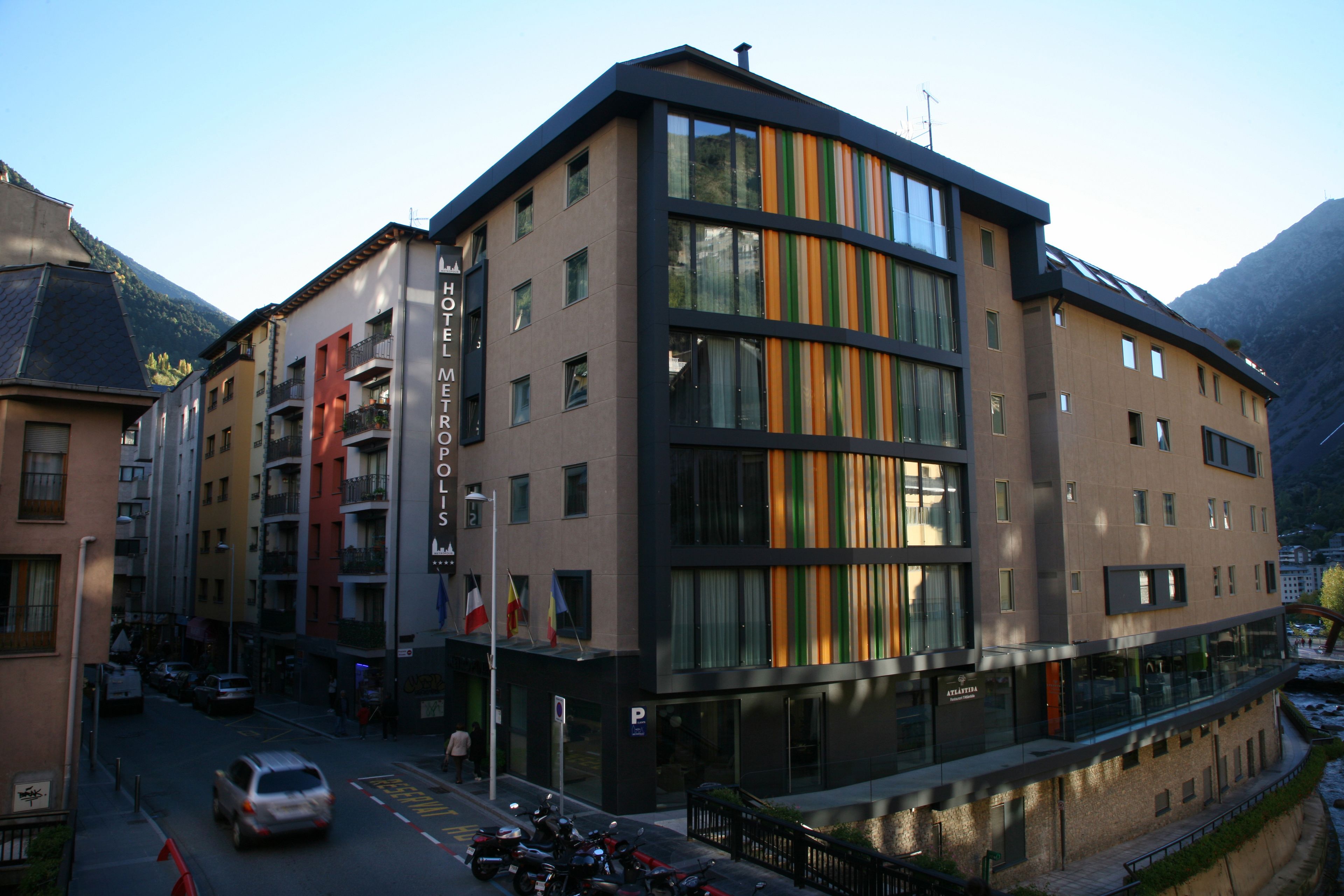 Un hotel moderno con un llamativo letrero de 'Hotel Mettrex', múltiples balcones y vistas al paisaje montañoso circundante.