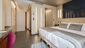 Una habitación de hotel moderna con una cama grande, un escritorio con una silla, y un baño visible a través de una puerta abierta.