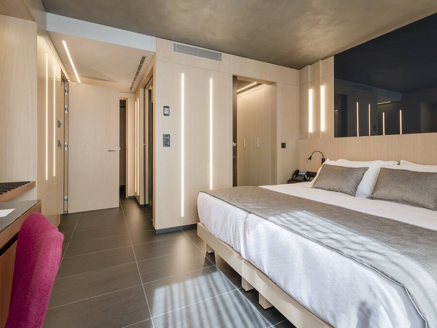 Ein modernes Hotelzimmer mit einem großen Bett, einem Schreibtisch mit Stuhl und einem durch eine offene Tür einsehbaren Badezimmer.