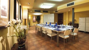 Un salón de conferencias con una larga mesa, sillas, una pizarra y una planta en maceta.