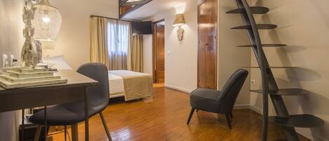 A hotel room with a bed, desk, chair, and a spiral staircase.