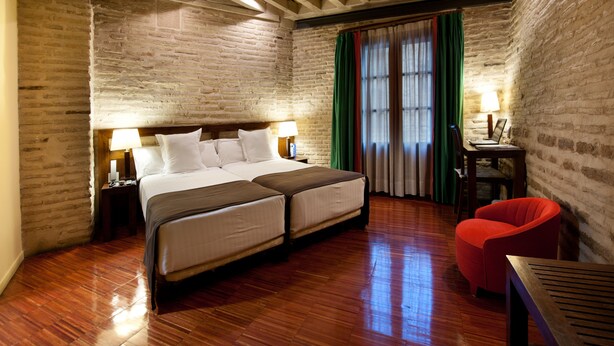 Habitación de hotel con una cama grande, suelo de madera, paredes de ladrillo y una silla roja.