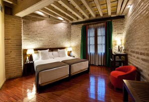 Habitación de hotel con una cama grande, suelo de madera, paredes de ladrillo y una silla roja.