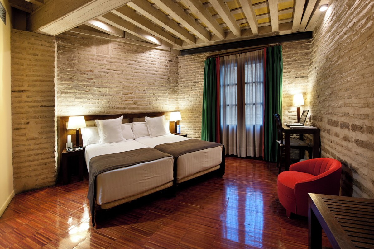 Habitación de hotel con una cama grande, suelo de madera, paredes de ladrillo y una silla roja.