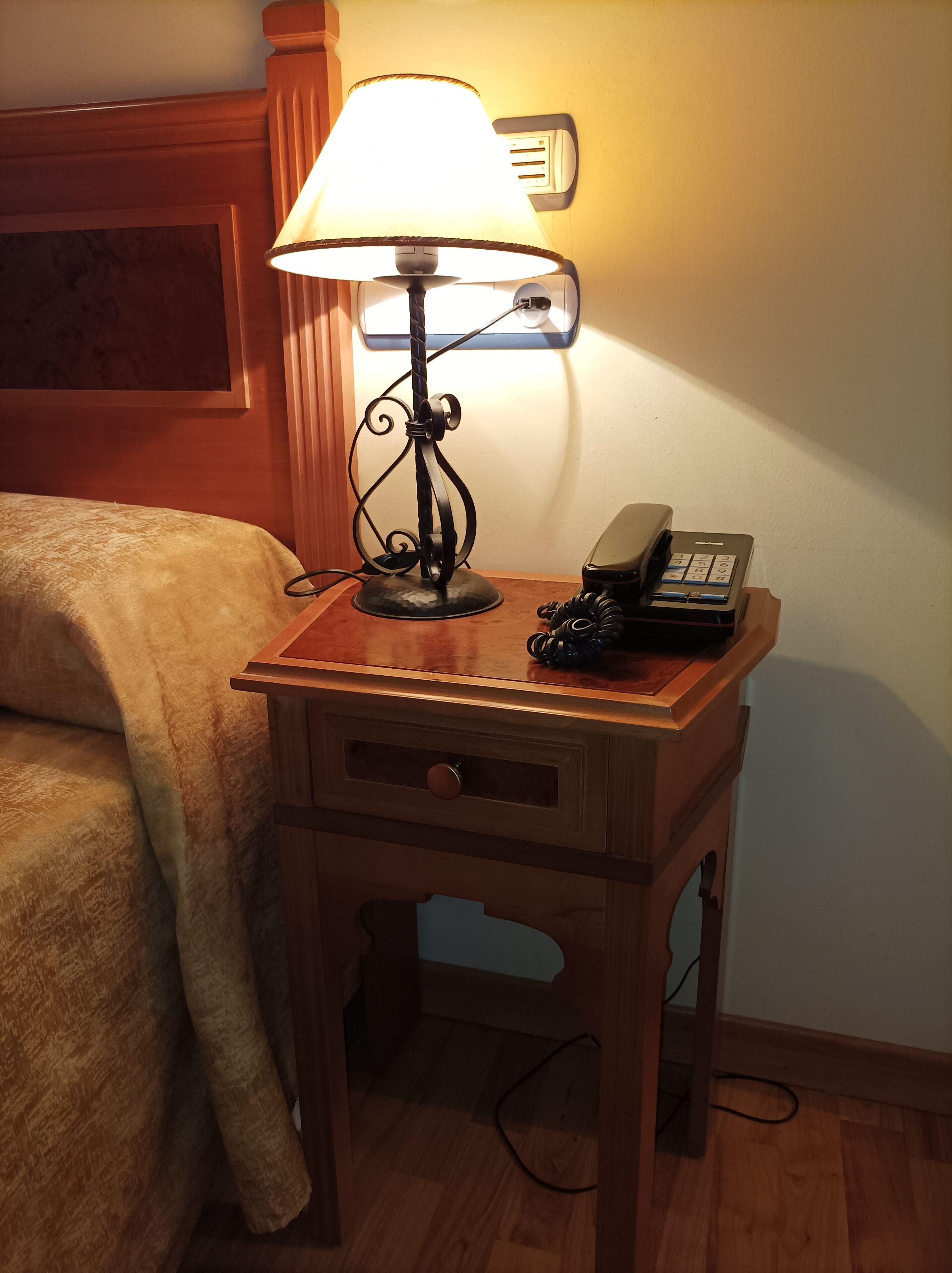 Un comodino in legno con una lampada, un telefono e un cassetto.
