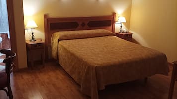 A hotel room with a wooden bed, two bedside tables with lamps, a wooden floor, and a framed picture on the wall.