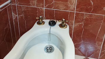 Un baño con un orinal blanco, baldosas de mármol rojo y un borde decorativo de azulejos.