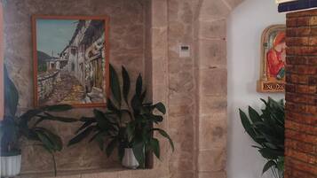 Un vestíbulo con piso a cuadros, pared de piedra, cuadro enmarco y plantas en macetas.