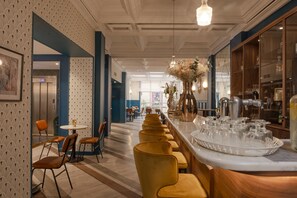 Zona de bar moderna con una barra larga, taburetes y un jarrón decorativo con flores.