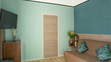A room with a light blue wall, a wooden cabinet, a brown sofa with teal pillows, and a flat-screen TV mounted on the wall.
