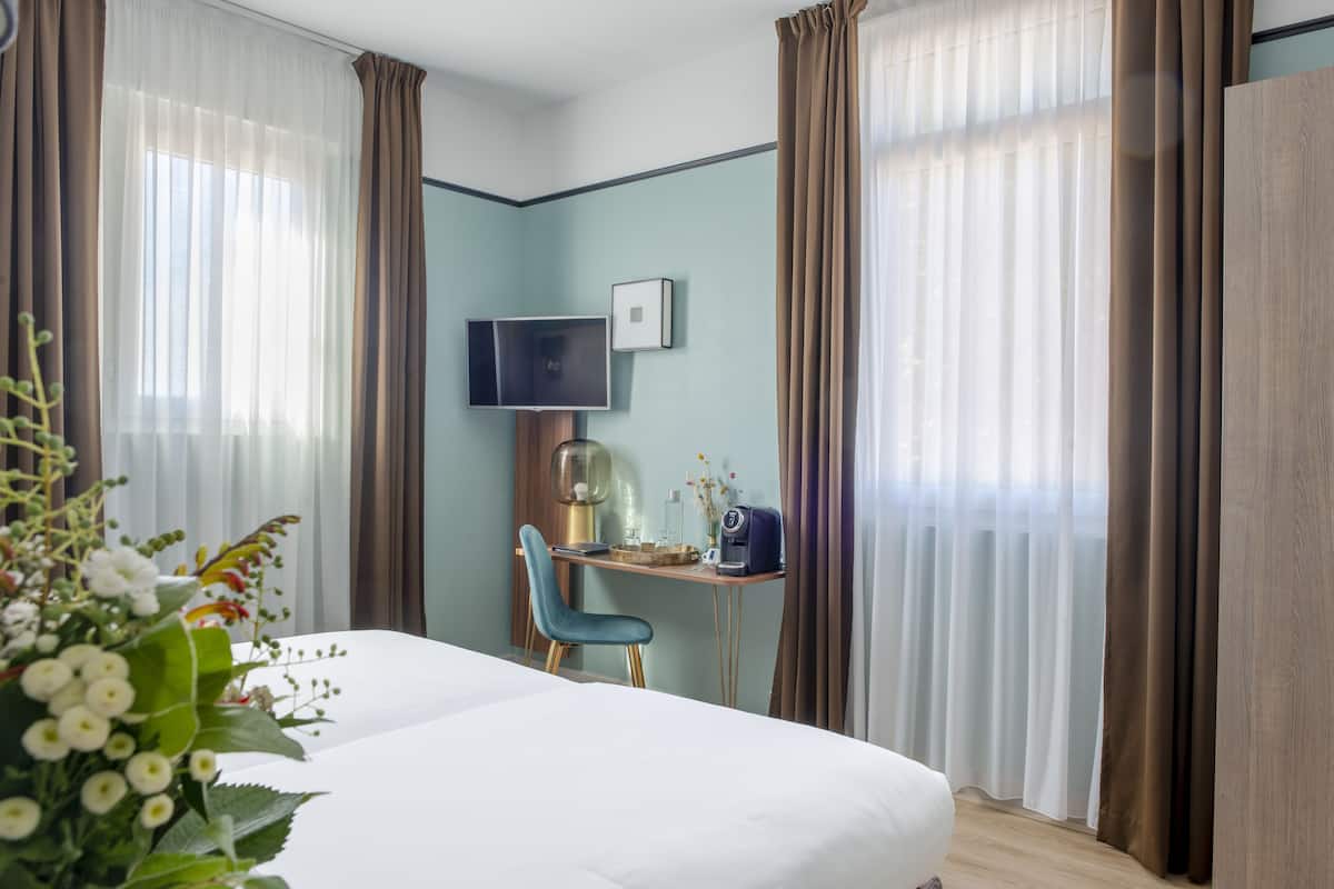 A hotel room with a bed, a desk with a chair, a television, and a window with curtains.