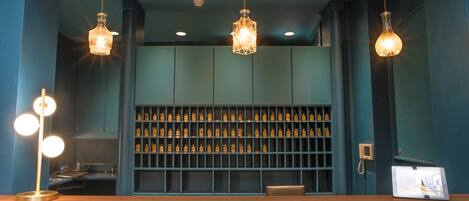 A bar area with a wooden counter, multiple hanging pendant lights, and a shelf with bottles.