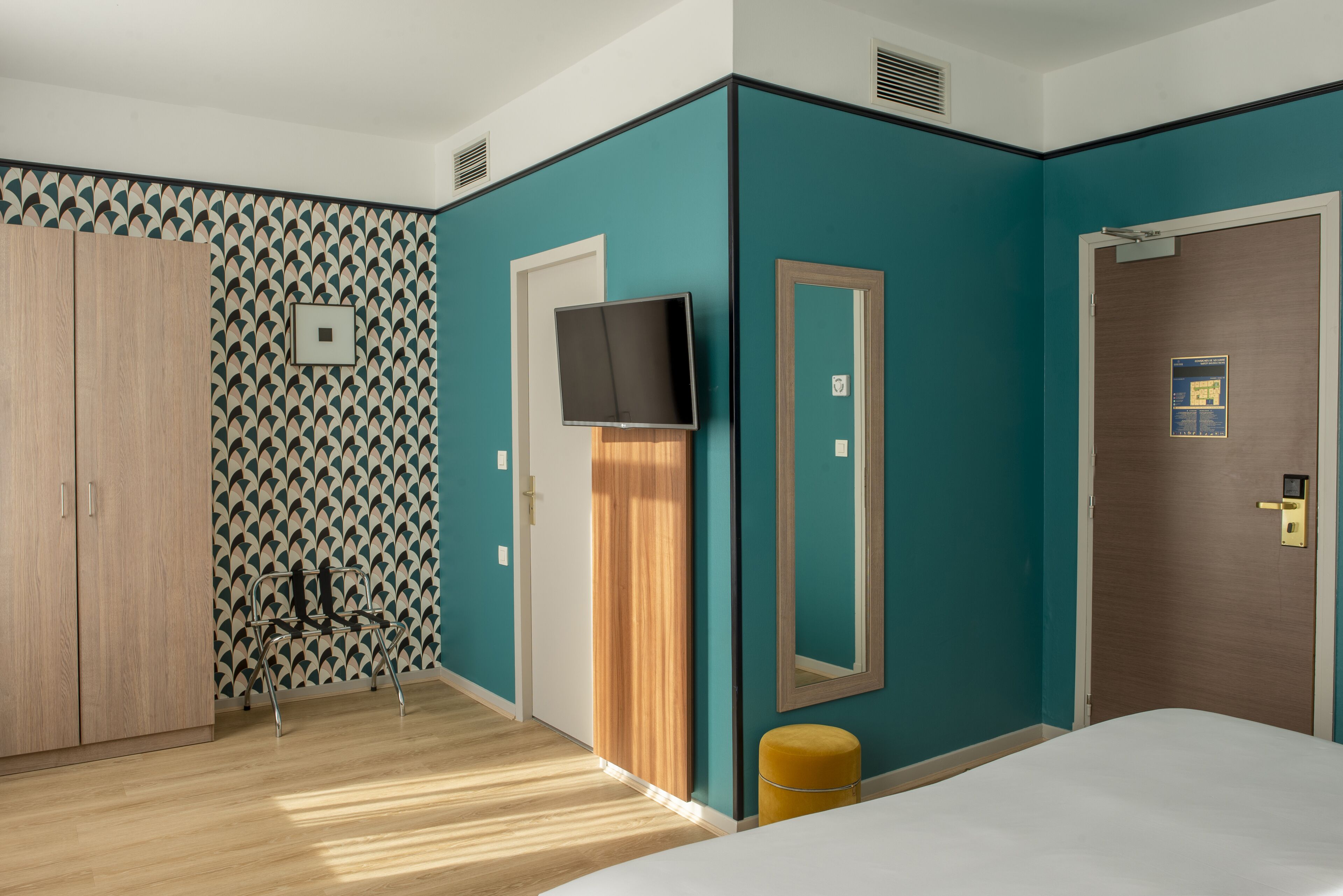Een hotelkamer met blauwgroene wanden, een houten garderobe, een televisie, een spiegel en een bed.