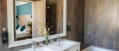 A modern bathroom with a large mirror, two sinks, a bathtub, and a shower.